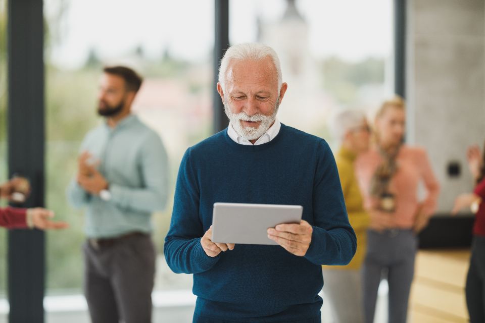 An older professional smiling at a tablet in a busy office